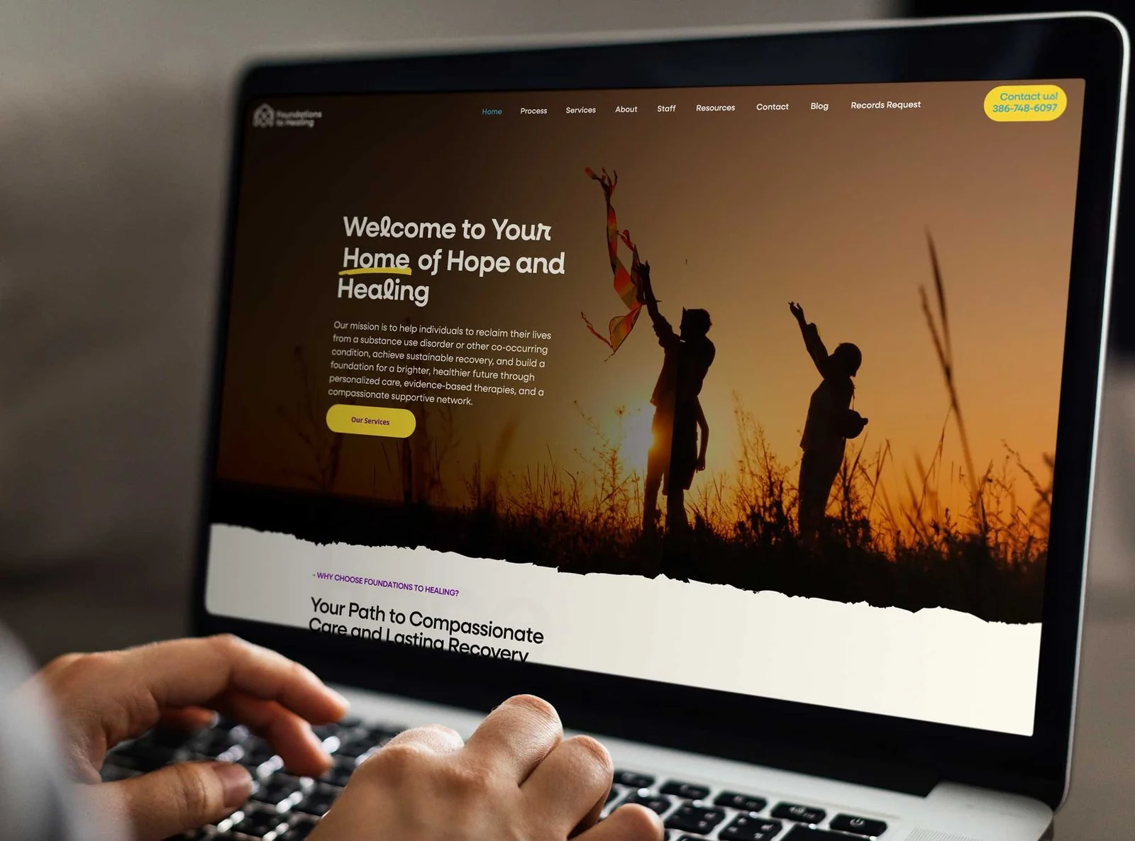 Laptop cu site-ul Foundations to Healing, cu o imagine de apus pe ecran